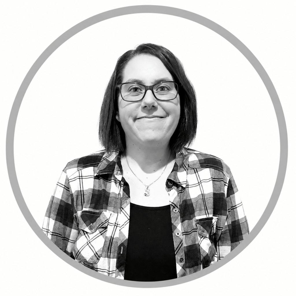Black-and-white head-and-shoulders portrait of a woman with glasses, wearing a plaid shirt and smiling.